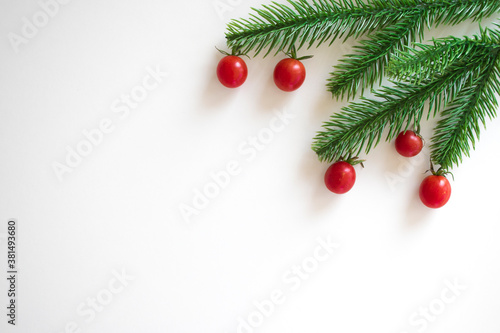 Christmas white background with fir branches and small red cherry tomatoes. Xmas, New Year's wallpaper. Winter holiday decorations isolated on white background with copy space. Flat lay, top view.
