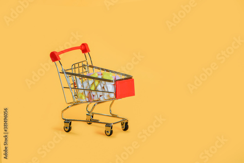 Small grocery cart with a bunch of white, pink and yellow pills,isolated on yellow background.Purchase of medicine