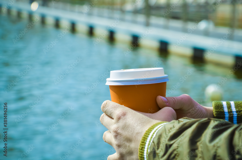 Female hands hold cardboard cup with coffee on the background of the sea pier. Relaxation by the sea, walks along the coast, takeaway coffee. Space for text. Female hands hold cardboard cup with coffee on the background of the sea pier. Relaxation by the sea, walks along the coast, takeaway coffee. Space for text.