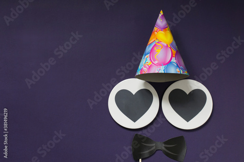 For a holiday for men. Postcard on a purple background - black bow tie, festive hat, two hearts for text. Copy space.