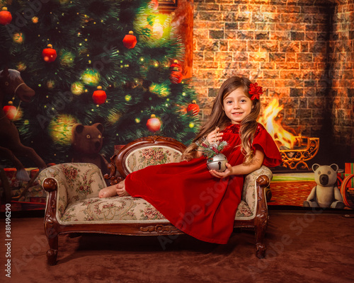 Christmas portrait of a little smiling girl wearing red costume playing with a toy on Christmas tree background © iryf