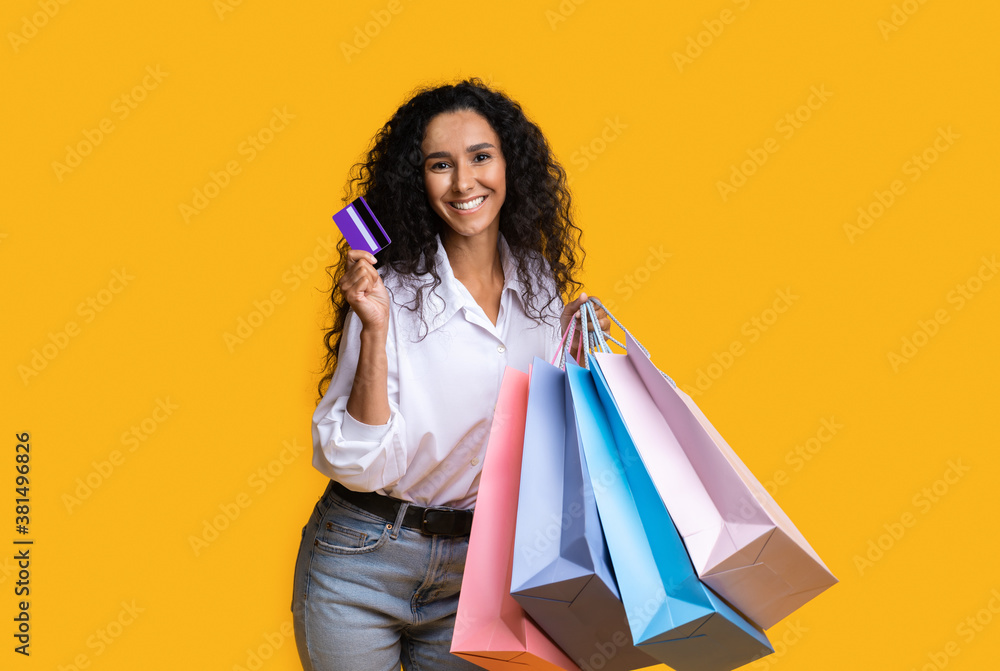 Shopaholic Woman Posing With Shopping Bags And Credit Card Over Yellow Background Shopaholic Woman Posing With Shopping Bags And Credit Card Over Yellow Background