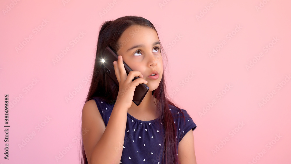 Fototapeta premium Little preschooler girl in a dress holding a mobile phone, isolated over pink