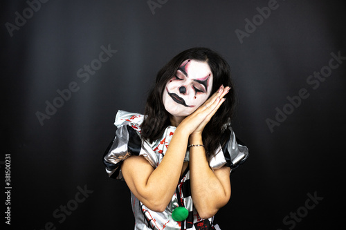 woman in a halloween clown costume over isolated black background sleeping tired dreaming and posing with hands together while smiling with closed eyes.
