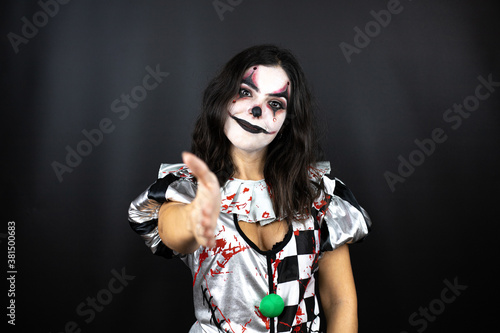 woman in a halloween clown costume over isolated black background smiling friendly offering handshake as greeting and welcoming