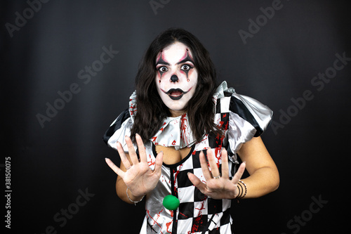 woman in a halloween clown costume over isolated black background afraid and terrified with fear expression stop gesture with hands, shouting in shock. Panic concept.