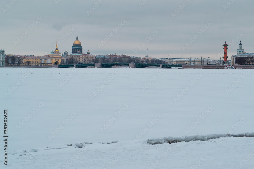 Winter embankment of Saint Petersburg with colored buildings and St. Isaac's Cathedral on banks of frozen Neva river in white snow with bridge. Light day