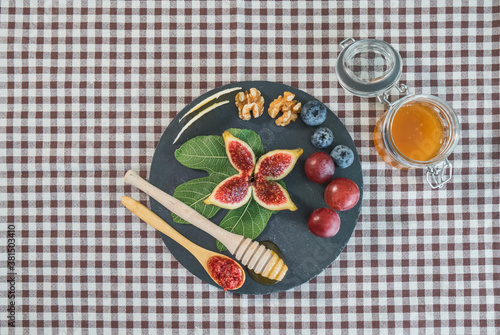 Figs, grapes and blueberries with cheese, honey and nuts in a slate dish on a rustic tablecloth, top view.