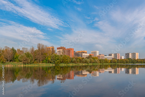 City landscape. Moscow. Residential area Izmailovo and its reflection in the pond in early autumn. View from Izmailovsky Island © Eselena