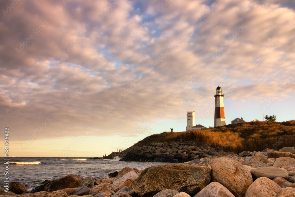 Warm golden light at sunset illuminating the side of a lighthouse sitting on a cliff. Montauk Point, New York