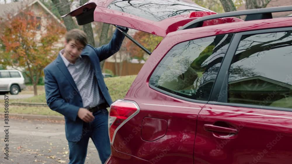 A goofy young man walking to the back of his red car, opening the trunk and struggling to pull out an oversized teddy bear, stumbling over himself. A goofy young man walking to the back of his red car, opening the trunk and struggling to pull out an oversized teddy bear, stumbling over himself.