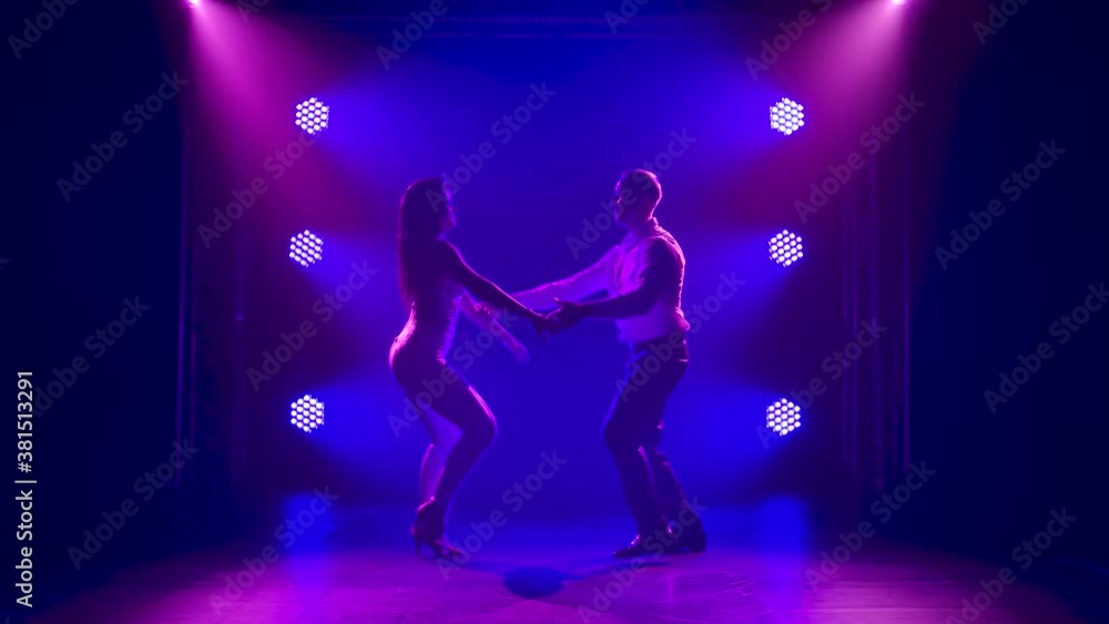 Young people dance to Latin American music at night. Salsa, bachata, rumba. Beautiful happy couple dancing salsa surrounded by blue lights in slow motion. Young people dance to Latin American music at night. Salsa, bachata, rumba. Beautiful happy couple dancing salsa surrounded by blue lights in slow motion.