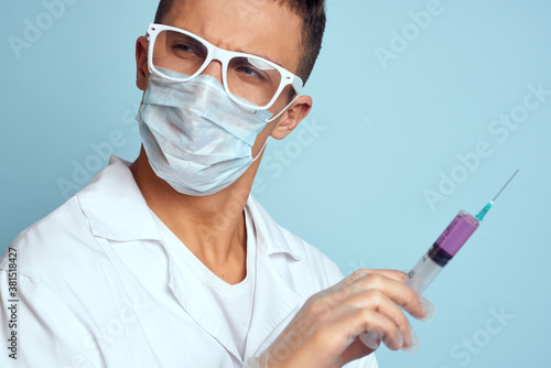 Doctor holds a syringe in his hand with a red liquid on a blue background medical gown and a protective mask