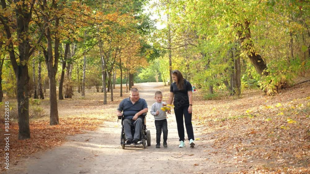 wheelchair man. Handicapped man. young disabled man in an automated wheelchair walks with his family, wife and small child, in the park, on sunny autumn day. wheelchair man. Handicapped man. young disabled man in an automated wheelchair walks with his family, wife and small child, in the park, on sunny autumn day.