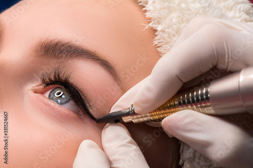 Permanent eye makeup close up shot. Cosmetologist applying tattooing of eyes. Makeup eyeliner procedure photo