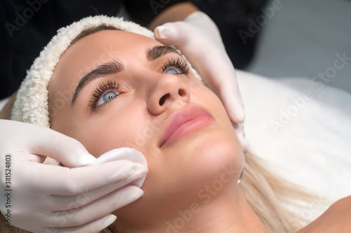 Young woman in a beauty salon. The beautician makes a facial cleansing procedure. Focus on eyes