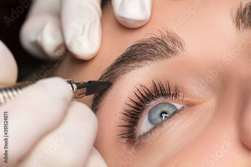 Permanent eyebrow makeup. Cosmetologist applying tattooing of eyebrows. Close up shoot