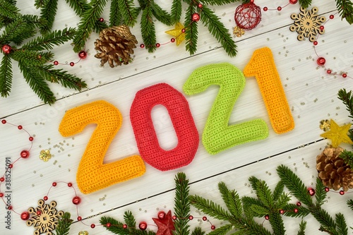 New year 2021, Christmas. Knitted colored numbers, fir branches and Christmas decorations on a white wooden background. Texture, design, decor, amigurumi, creativity, hobby, greeting card, handmade.