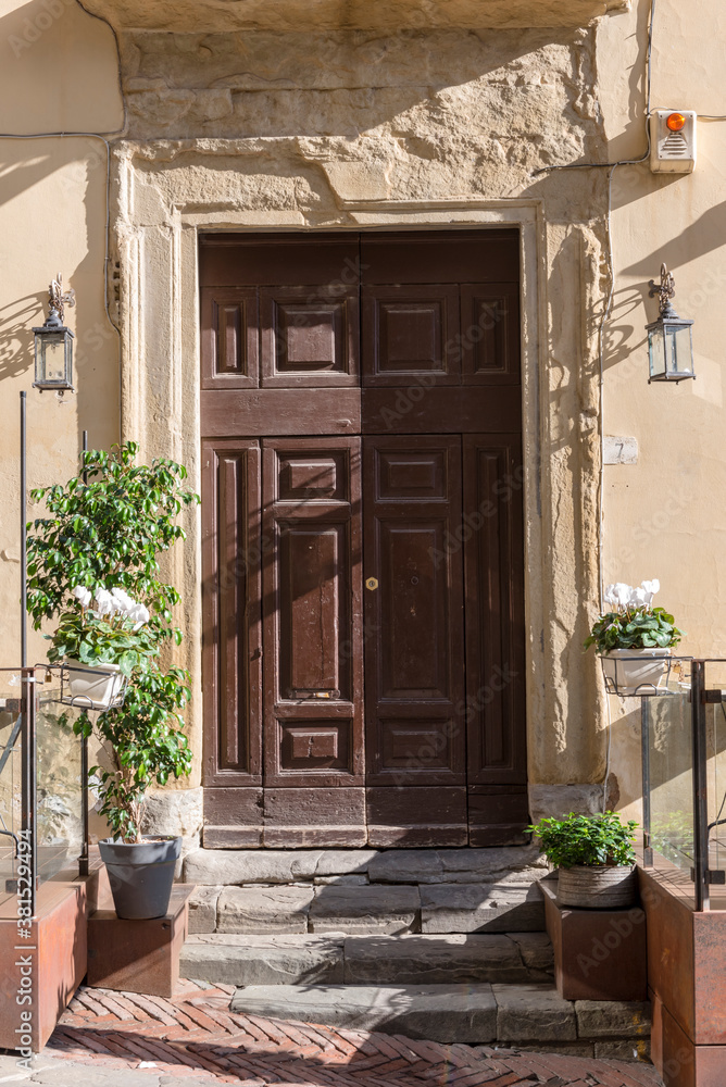 Fototapeta premium The door to the multi-storey house from the street in the Italian city of Arezzo. Pots of flowers tied to a chain with locks so that passers-by did not take them
