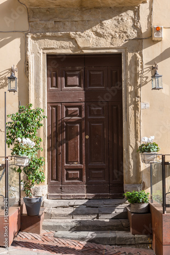 The door to the multi-storey house from the street in the Italian city of Arezzo. Pots of flowers tied to a chain with locks so that passers-by did not take them