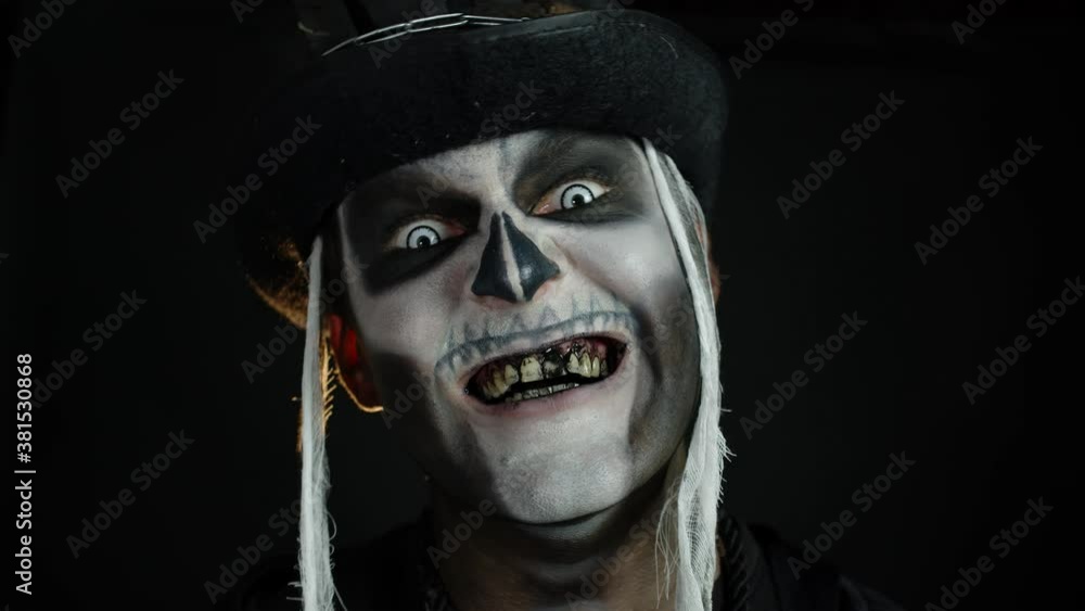 Creepy man face with skeleton makeup in top-hat appearing on black background. Halloween party Creepy man face with skeleton makeup in top-hat appearing on black background. Halloween party