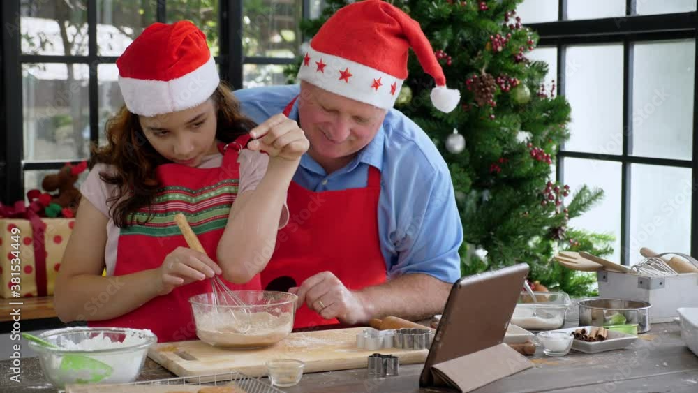 Father & Daughter making video call during making ginger beard cookie for christmas concept. Handheld, medium shot of young girl grabs and moves a tablet to closer, then poses salt pinching to camera Father & Daughter making video call during making ginger beard cookie for christmas concept. Handheld, medium shot of young girl grabs and moves a tablet to closer, then poses salt pinching to camera