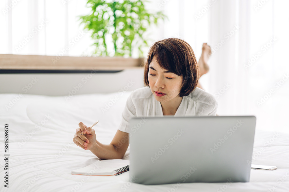 Smiling happy beautiful asian woman relaxing using laptop computer working and video conference meeting on bed at home.work from home concept Smiling happy beautiful asian woman relaxing using laptop computer working and video conference meeting on bed at home.work from home concept