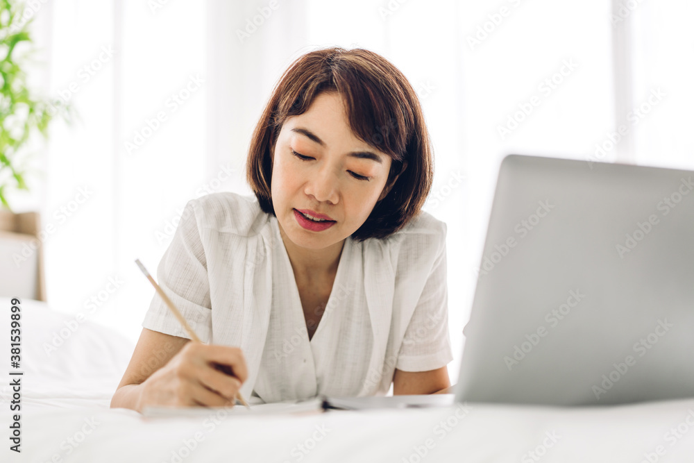 Smiling happy beautiful asian woman relaxing using laptop computer working and video conference meeting on bed at home.work from home concept Smiling happy beautiful asian woman relaxing using laptop computer working and video conference meeting on bed at home.work from home concept