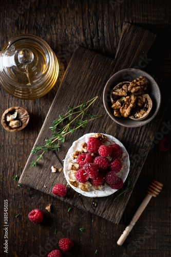 brie or camembert cheese with raspberries  honey and walnuts . Selective focus  dark background  top view