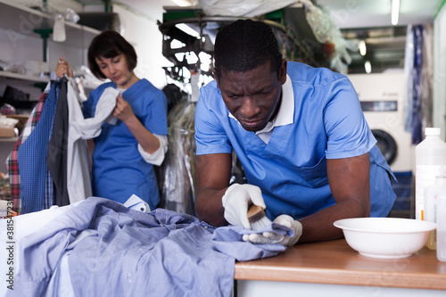 Focused African-American man dry cleaning clothes in laundry ..