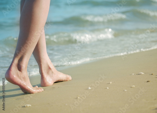 Woman feet walking barefoot on sandy beach of sea.