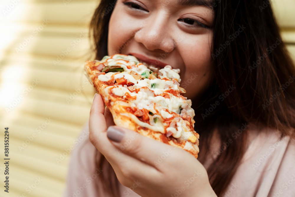 Asian chubby woman eating a piece of pizza. Asian chubby woman eating a piece of pizza.