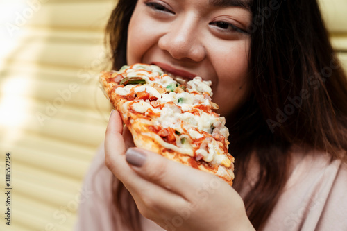 Asian chubby woman eating a piece of pizza.