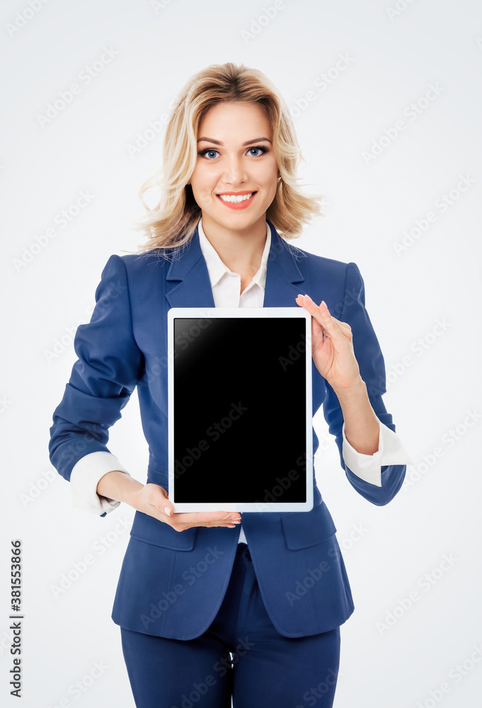 Smiling young businesswoman in blue confident suit, showing blank no-name tablet pc monitor with copy space area for text, isolated on grey background. Caucasian blond model in business concept. Smiling young businesswoman in blue confident suit, showing blank no-name tablet pc monitor with copy space area for text, isolated on grey background. Caucasian blond model in business concept.