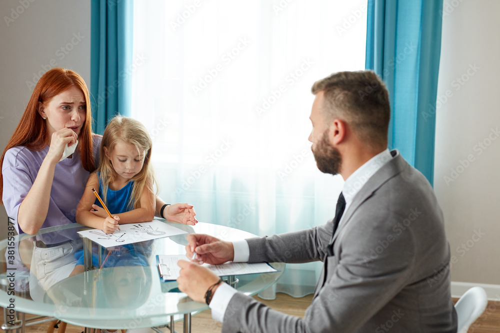 Obraz premium young depressed caucasian woman with child girl get support by psychologist, they sit at table talking, woman with red hair explain her problem and situation