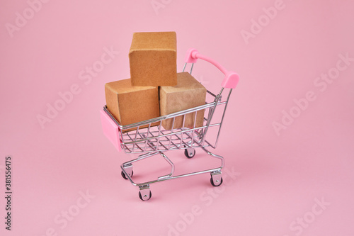 Shopping cart with package boxes on pink background. Shopping and delivering concept. Shop trolley full of parcels.