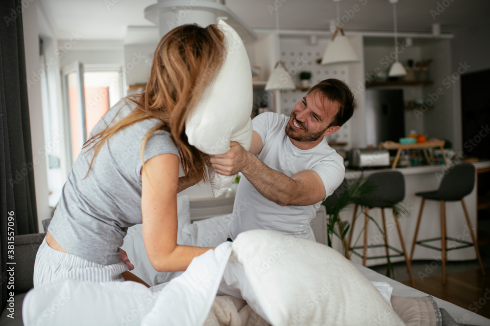 Fototapeta premium Young couple fighting pillows on the bed. Happy couple having fun at home.