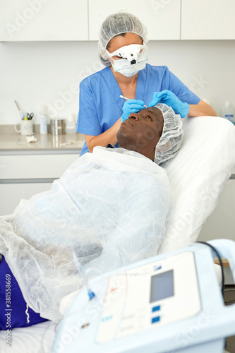 Dermatologist female preparing man client before aesthetic facial procedure in medical office