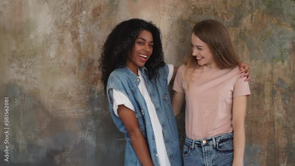 Black girl and caucasian young woman hug each other with affection. Two loving friends laugh together. Medium shot. Black girl and caucasian young woman hug each other with affection. Two loving friends laugh together. Medium shot.