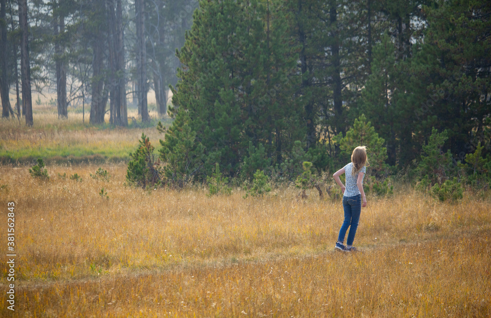 Girl playing hide and seek in grass fields next to a forset. lady back. Growing sunlight blonde hair.
