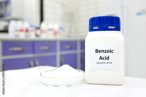 Selective focus of a bottle of pure benzoic acid chemical compound beside a petri dish with solid crystalline powder substance. White Chemistry laboratory background with copy space. photo