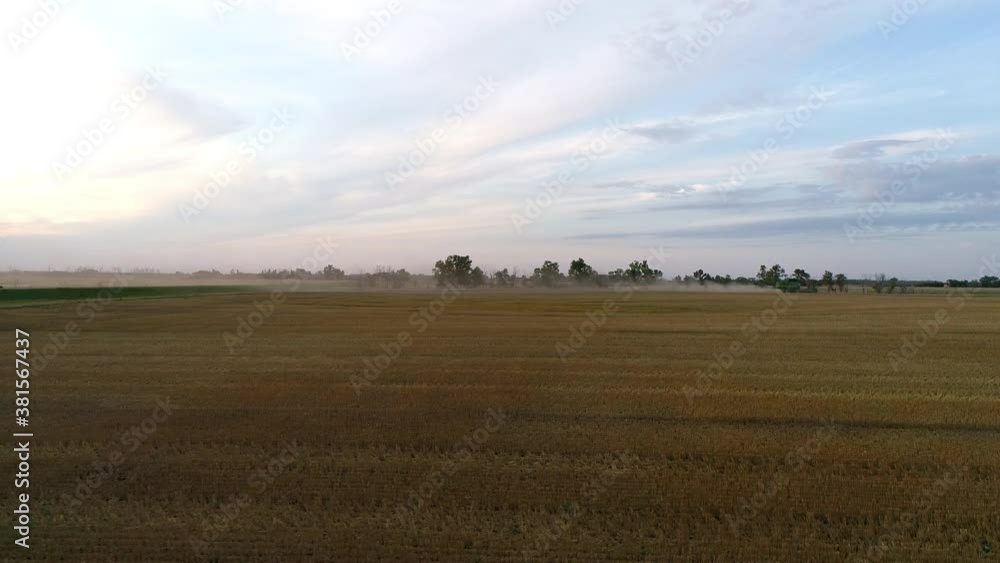 Side view tracking along a field with a combine harvester in the background at sunset.