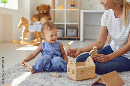 Joyful young nanny and little kid playing with wooden blocks in cozy nursery room photo