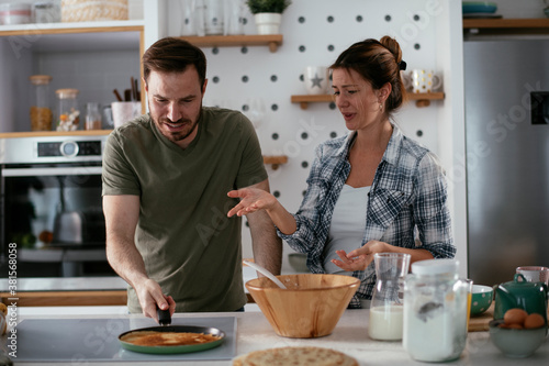 Fototapeta Naklejka Na Ścianę i Meble -  Young couple making pancakes at home. Loving couple having fun while cooking
