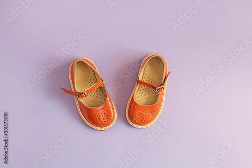 Bright orange kids shoes on lilac background with copyspace. Baby clothes concept. Top view, flat lay