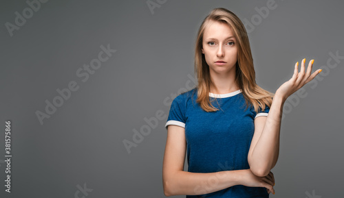 Portrait of beautiful blonde girl looking at camera suspiciously. Studio shot, gray background. Copy space