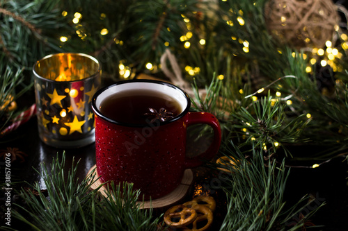 New year's tea party with spices. Red mug with tea surrounded by garlands, fir branches and spices   © SVETLANA