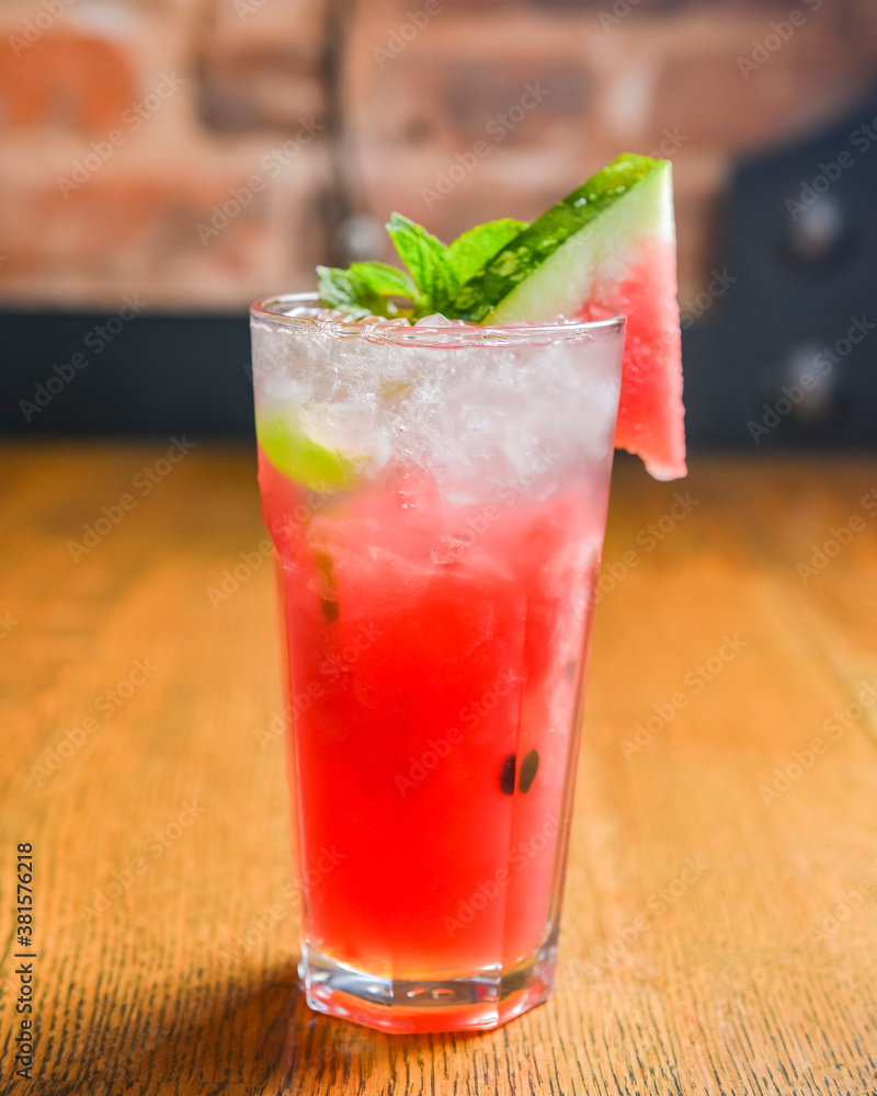 Watermelon smoothie garnished with watermelon slices and mint leaves served in a glass on rustic wooden table. Watermelon smoothie garnished with watermelon slices and mint leaves served in a glass on rustic wooden table.