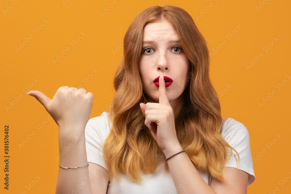 Pretty girl asking to be quiet with finger on lips pointing with hand to the side. Silence and secret concept Pretty girl asking to be quiet with finger on lips pointing with hand to the side. Silence and secret concept