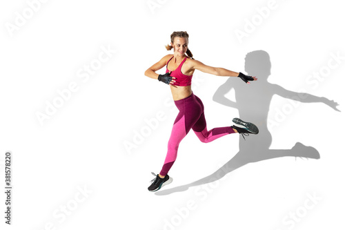 Strong. Beautiful young female athlete practicing on white studio background, portrait with shadows. Sportive fit model in motion and action. Body building, healthy lifestyle, style concept.